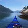 The front of a kayak gliding through the waters of a fjord toward 2 other kayakers